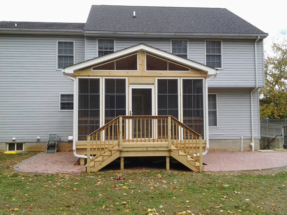 wood deck built by Nevins Construction with a screen in room and a landing with steps on both sides that lands on a paver patio on both sides of the deck